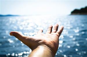 Hand stretching toward the horizon above the ocean 